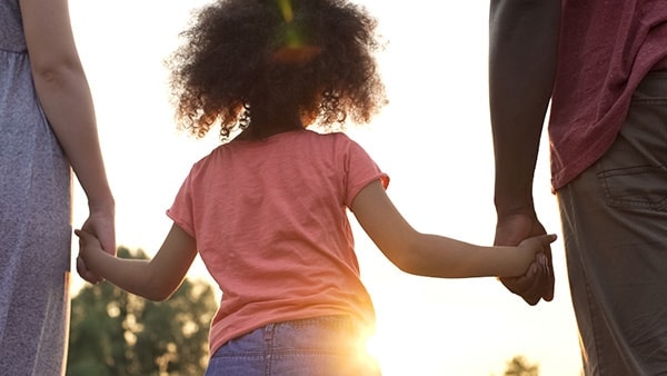 Child holding hands with two parents at sunset